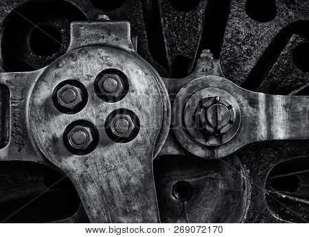 Close Up Of The Wheel And Coupling Rods Of An Old Steam Locomotive With Textured Metal Surface And B