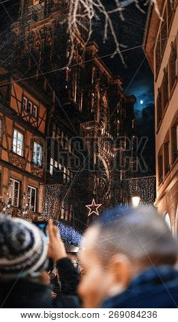 Adult Male Couple Taking Photo On Smartphone Of Notre-dame Cathedral And Maison Kammerzell Decorated