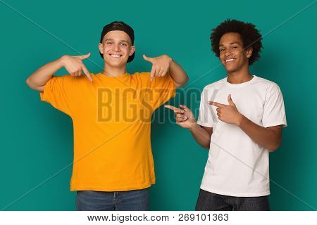Diverse Teens Pointing At Blank T-shirt Over Blue Background, Copy Space