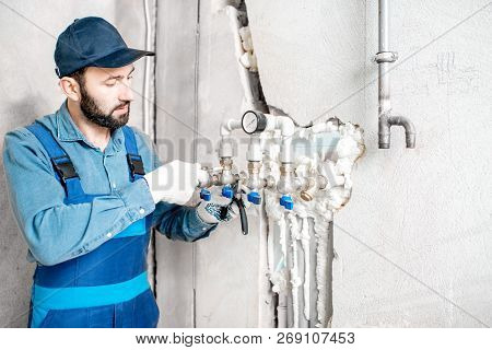 Workman In Blue Uniform Installing Water Heating System On The Construction Site Of A New House