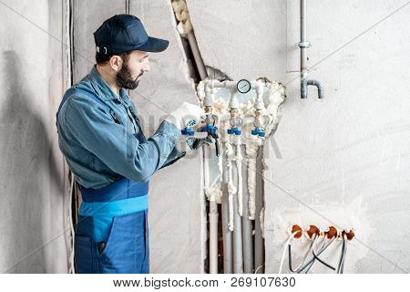 Workman In Blue Uniform Installing Water Heating System On The Construction Site Of A New House