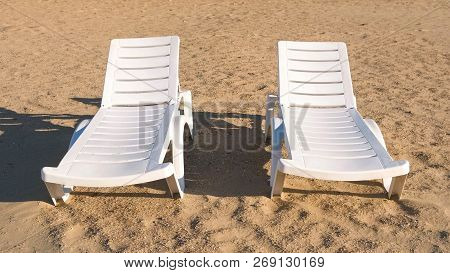 Two Sunlongers On The Sand Beach In Summer.