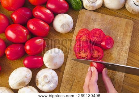 Womans Hands Is Cutting Tomatoes On The Wooden Bord On Kitchen Table. Side View.