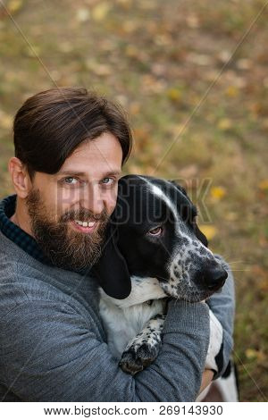 Young Man With Dog Walks In Autumn Park. He Hugged His Pet. Dog Is Hunting, Short-footed, Lop-eared 