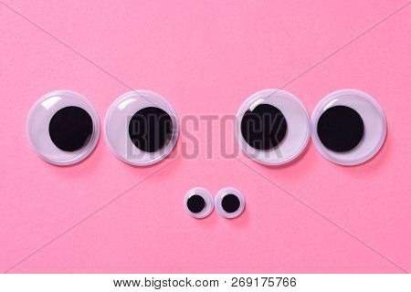 Googly Eyes Of Family Of Two People With Child On Rose Background. Close Up.