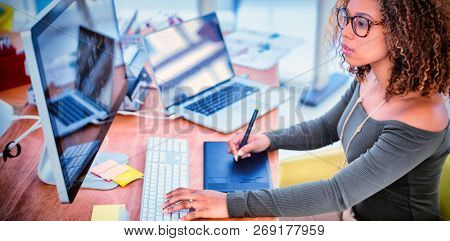 Female graphic designer working on computer while using graphic tablet at desk in the office