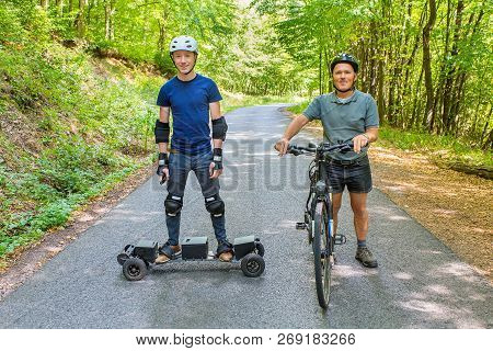 Father And Son Standing With Mountain Bike And Mountainboard On Road