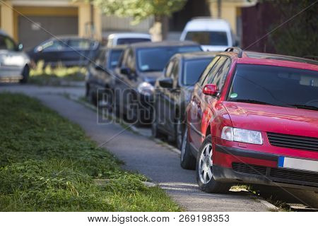 Front View Of Red Car Parked Partly On Sidewalk On Background Of Long Row Of Different Vehicles Alon