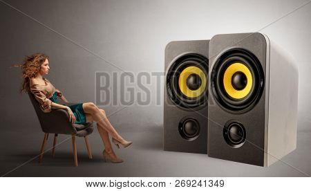 Stylish young lady sitting in a sofa and listening to big loudspeakers