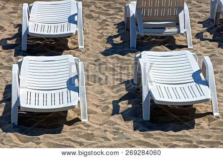 White Plastic Loungers Are Standing On The Sand Of The Beach