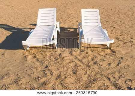 Two Sunlongers On The Sand Beach In Summer.