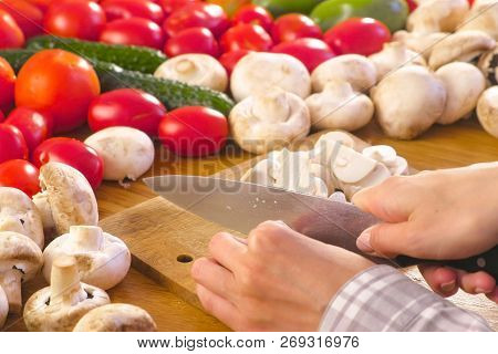Womans Hands Is Cutting Mushrooms Champignons On The Wooden Bord On Kitchen Table.