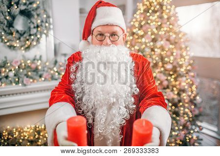 Santa Claus Stands Alone In Room And Holds Two Red Candles In Habds. He Shows Them On Camera. Man Is