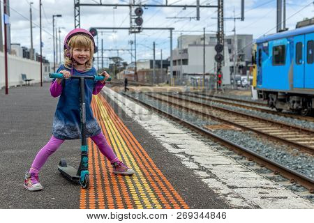 Young Girl In Pink Outfit And Pink Helmet Riding A Kick-scooter Across The Railway Line