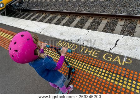 Young Girl In Pink Outfit And Pink Helmet Riding A Kick-scooter Across The Railway Line