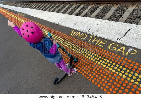 Young Girl In Pink Outfit And Pink Helmet Riding A Kick-scooter Across The Railway Line