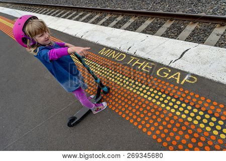 Young Girl In Pink Outfit And Pink Helmet Riding A Kick-scooter Across The Railway Line