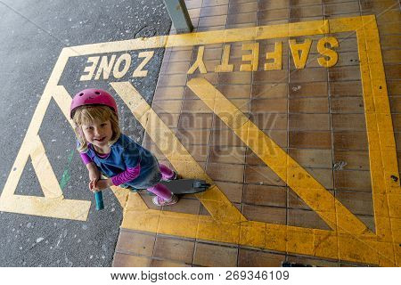 Young girl in pink outfit and pink helmet riding a kick-scooter across the railway line