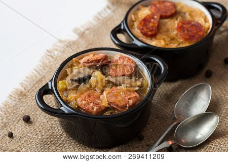 Slovak Christmas National Cabbage Soup In Two Small Black Pots With Sausage On The Tablecloth Backgr