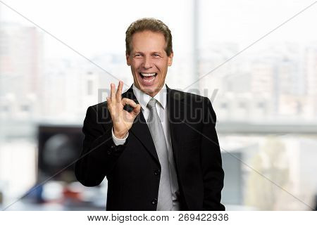Joyful Businessman Showing Ok Sign. Happy Cheerful Executive Gesturing With Fingers Ok On Blurred Ba