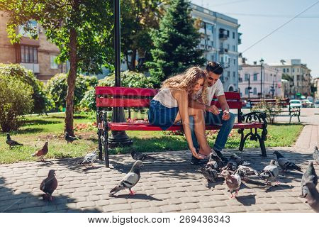 Young Mixed Race Couple In Love Feeding Bidrs In Summer Park. Man And Woman Thowing Bread To Doves