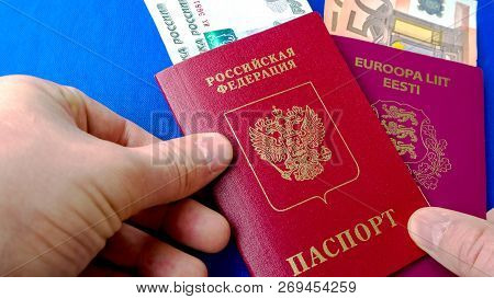 Hands Holding Passports On Blue Background. Citizenship Of Estonia And Russia. Citizenship Of Europe