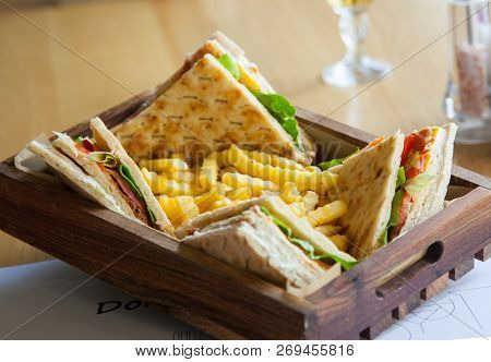 Four Small Sandwiches And French Fries In A Wooden Plate On A Table.