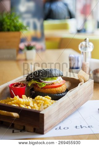 Black Colored Small Mouth-watering, Delicious Burger On The Wooden Tray Served With Red Ketchup Sauc