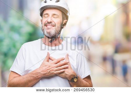 Middle age senior hoary cyclist man wearing bike safety helment isolated background smiling with hands on chest with closed eyes and grateful gesture on face. Health concept.