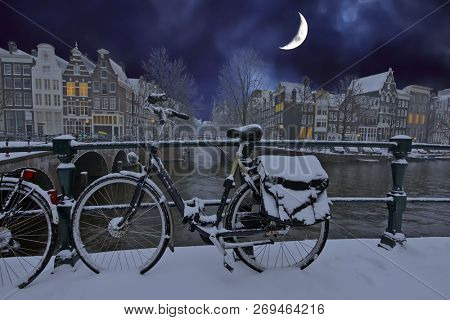City scenic from snowy Amsterdam in the Netherlands in winter at night with half moon