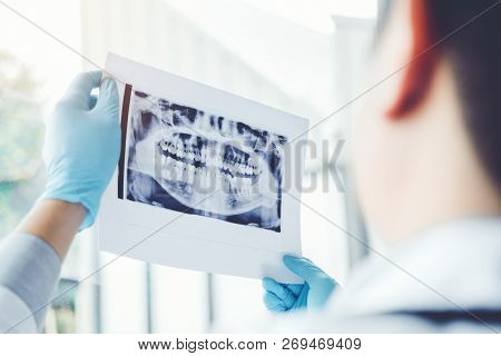 Dentist Consulting With Patient Presenting Results On Dental X-ray Film About The Problem Of The Pat