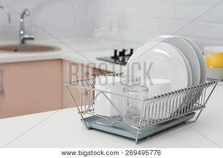 Dish Drainer With Clean Dinnerware On Table In Kitchen. Space For Text