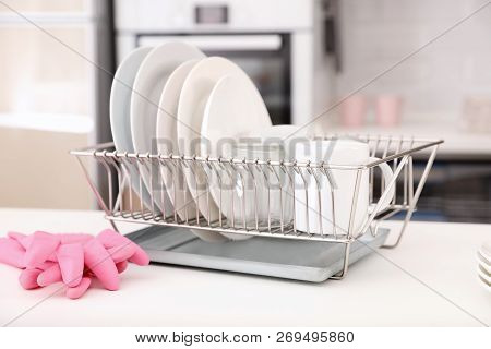 Dish Drainer With Clean Dinnerware On Table In Kitchen