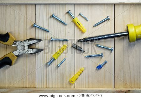 Screws, Dowels, Screwdriver And Pliers Lie On A Wooden Surface. Locksmith Work With Wood.
