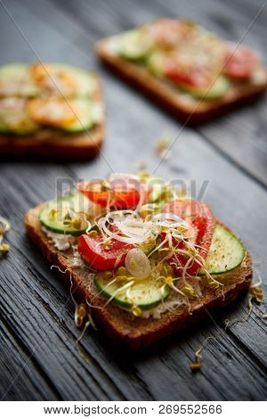 Healthy vege toasts with onion, cucomber, cherry tomatoes, crumbled feta cheese and radish sprouts. Table top view on black wooden background