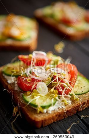 Healthy vege toasts with onion, cucomber, cherry tomatoes, crumbled feta cheese and radish sprouts. Table top view on black wooden background