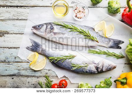 Fresh Raw Seabass And Ingredients For Cooking. Two Fish Seabass With Lemon, Spices And Herbs On Wood