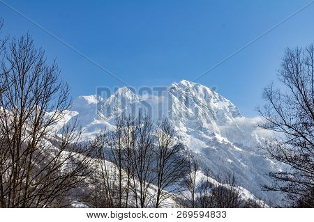 Near Balnea Spa In The French Pyrenees, A Snow Covered Peak Rises Above The Surrounding Trees