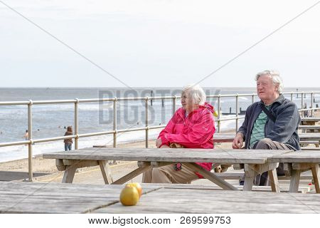 Southwold, Uk - September 8, 18 - Senior Couple Sitting On The Seaside Table Bench Looking Over The 