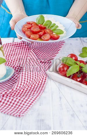 A Woman Is Holding A Plate With A Traditional Italian Salad Caprese. Tomatoes And Mazarella Cheese. 