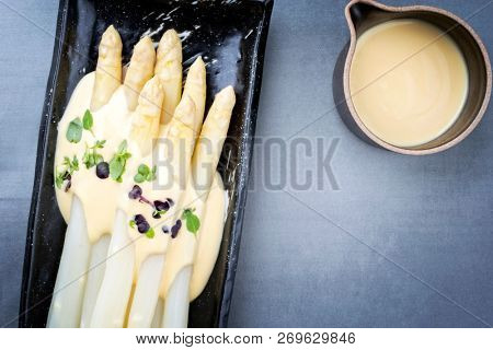 Traditional boiled white asparagus with sauce hollandaise and herbs as top view on a plate with copy space right 