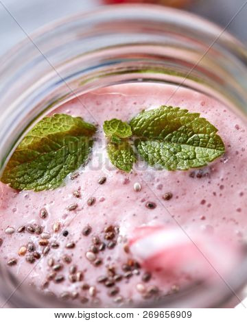 Appetizing milky berry smoothie with mint leaves and organic chia seeds in a glass with a straw. Healthy dessert. Top view