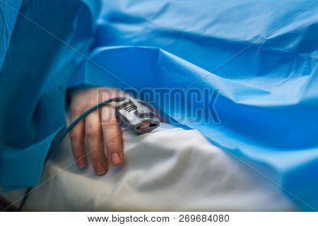 Detail of a hand of a patient being monitored dusing surgery - vital functions of the body are being closely watched by the anaesthesiologist (color toned image, shallow DOF)