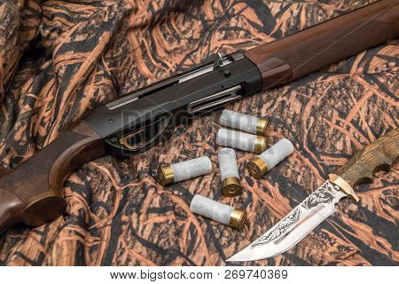 Shotgun, Hunter Knife, Cartridges And Ammunition Belt On The Camouflage Background