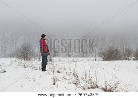 Man Is Standing Along In Peace And Harmony With Nature. He Is Wathing In A Winter Snowy Landscape Wi