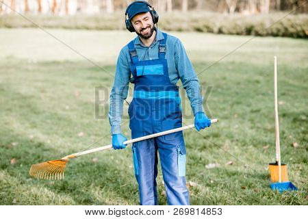 Professional Male Sweeper Or Gardener In Uniform Listening To The Music With Headphones While Cleani