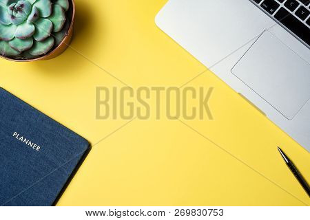 Flatlay Of Work Place Silver Laptop Secculent Plant And Blue Organizer Over Yellow Background