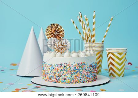 Delicious Cake, Plactic Cups, Party Hats And Drinking Straws On Blue Background With Confetti