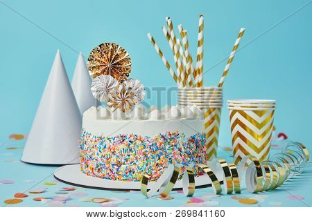 Cake, Party Hats, Plactic Cups, Golden Paper Streamer  And Drinking Straws On Blue Background With C