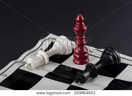Three Chess Kings Standing In Front Of Each Other, White And Black Kings Fallen, Red King Standing B